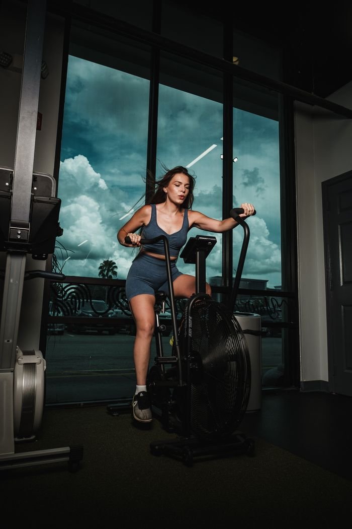 Services A woman works out on a stationary bike indoors, promoting fitness and health.