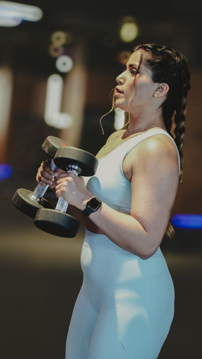 Mastering the First Impression: Your intriguing post title goes here A focused woman lifting dumbbells during a workout in a gym, showcasing strength and fitness.