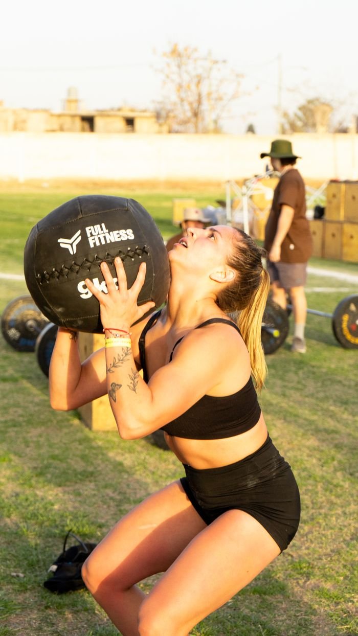 Young woman lifting a medicine ball outdoors during a fitness workout session.